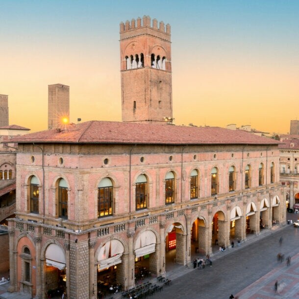 Historische Gebäude mit Arkaden und Turm am Piazza Maggiore in Bologna bei Sonnenuntergang