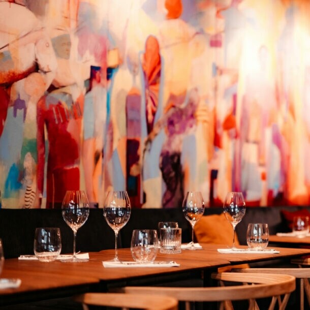 Mehrere eingedeckte Holztische vor einem bunten, großflächigem Wandbild.