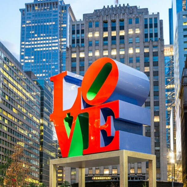 Skulptur mit dem Schriftzug 'LOVE' in roten und grünen Buchstaben vor Hochhäusern in einer Stadt