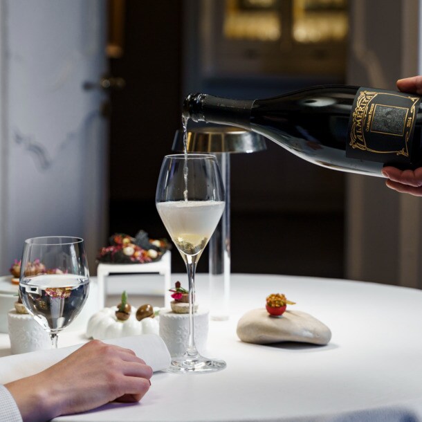 In einem Restaurant mit tiefblauen Wänden schenkt ein Kellner edlen Schaumwein in ein Glas ein.