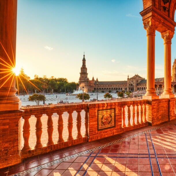 Überdachte Promenade an einem halbkreisförmigen Palastkomplex im andalusischen Stil an einem großen Platz im warmen Licht bei Sonnenuntergang.