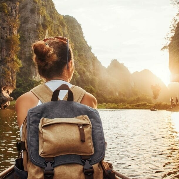 Frau mit Rucksack sitzt in einem Kanu auf einem Fluss, umgeben von hohen Felsen bei Sonnenuntergang.