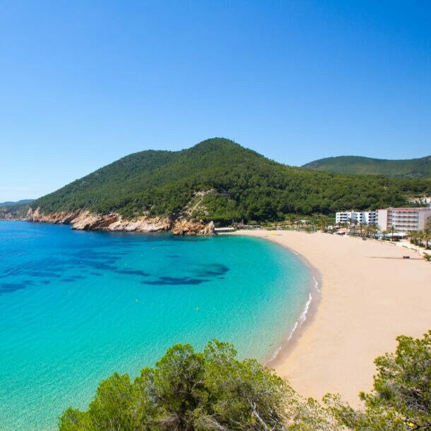 Bucht mit türkisfarbenem Wasser, Sandstrand und bewaldeten Hügeln unter klarem Himmel
