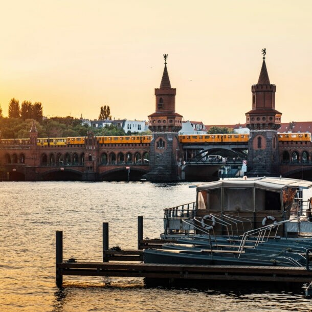 Sonnenuntergang über der Oberbaumbrücke in Berlin mit vorbeifahrender U-Bahn und Booten auf der Spree.