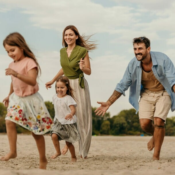 Familie mit zwei Kindern läuft barfuß am Strand bei bewölktem Himmel