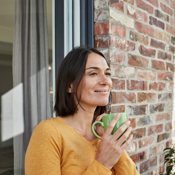 Eine Frau mit einer Tasse in der Hand lehnt entspannt an der Hauswand.