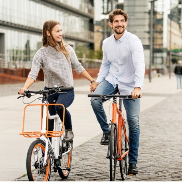 Paar hält Händchen beim Fahrradfahren auf einem gepflasterten Weg in einem modernen Stadtviertel