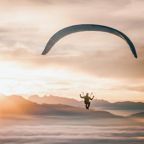Person beim Gleitschirmfliegen über neblige Berglandschaft bei Sonnenaufgang