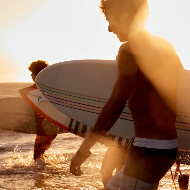 Drei Surfer mit Surfboards laufen bei Sonnenuntergang ins Wasser am Strand
