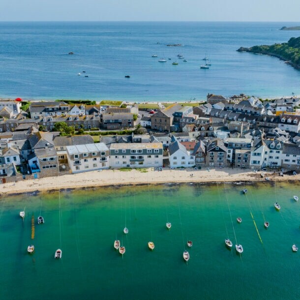 Luftaufnahme eines Küstendorfes mit weißen Häusern, einem Sandstrand und zahlreichen Booten im klaren, grünen Wasser einer Bucht