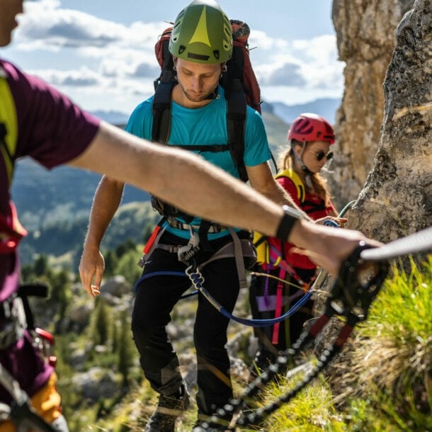 Drei Personen in Kletterausrüstung an einem Felsen mit Drahtseil.