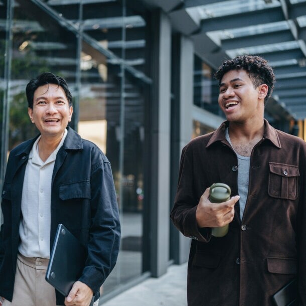 Zwei Kollegen spazieren gemeinsam und halten dabei eine Projektbesprechung ab.