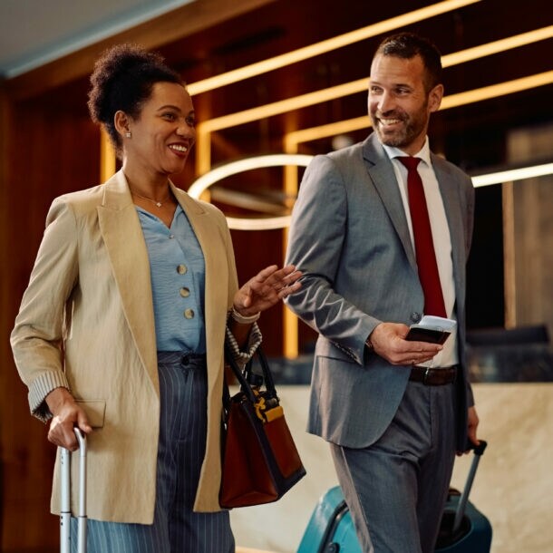 Eine Frau und ein Mann in Business-Kleidung mit Trolleys gehen gut gelaunt durch eine Hotellobby.