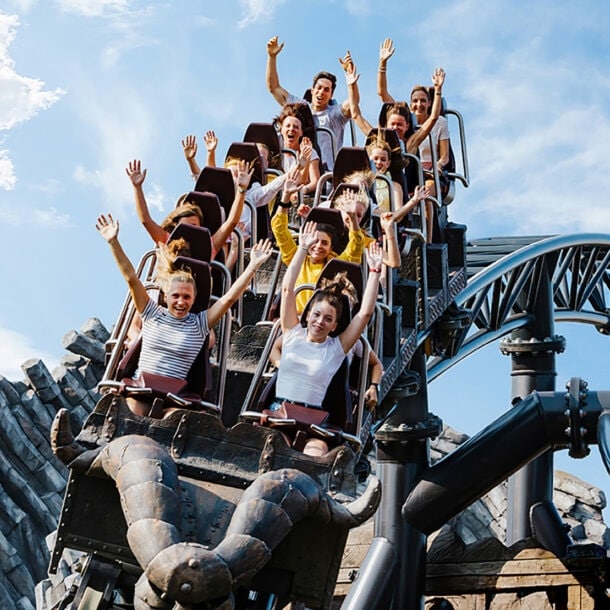 Menschen fahren auf der Achterbahn Taron im Phantasialand, Arme in die Luft gestreckt, vor blauem Himmel