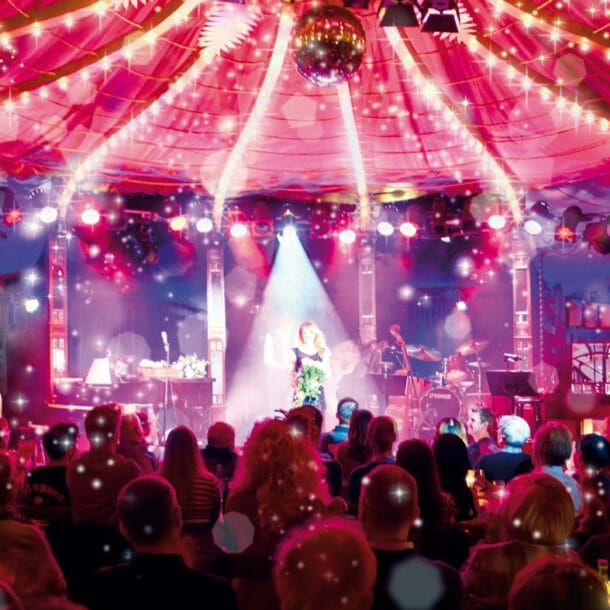 Bühne im Bar jeder Vernunft Theater Berlin mit Künstlerin im Scheinwerferlicht vor Publikum unter Zelt mit Lichterketten