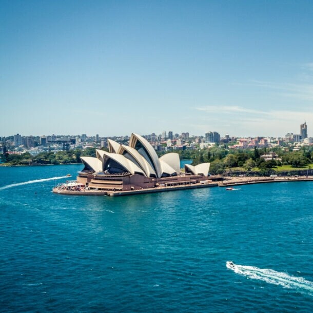 Sydney Opernhaus am Hafen mit Boot auf blauem Wasser und Hochhäusern im Hintergrund