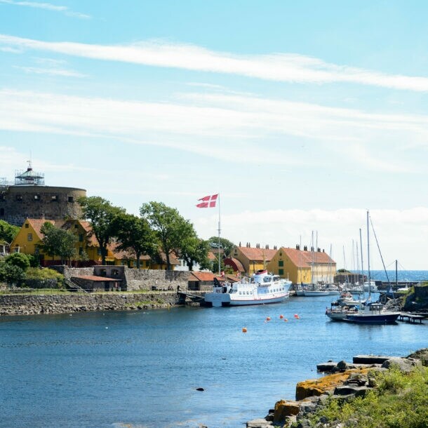 Hafen mit Segelbooten und Fähre, dänische Flagge weht, historische Festung und Häuser am Ufer auf Bornholm