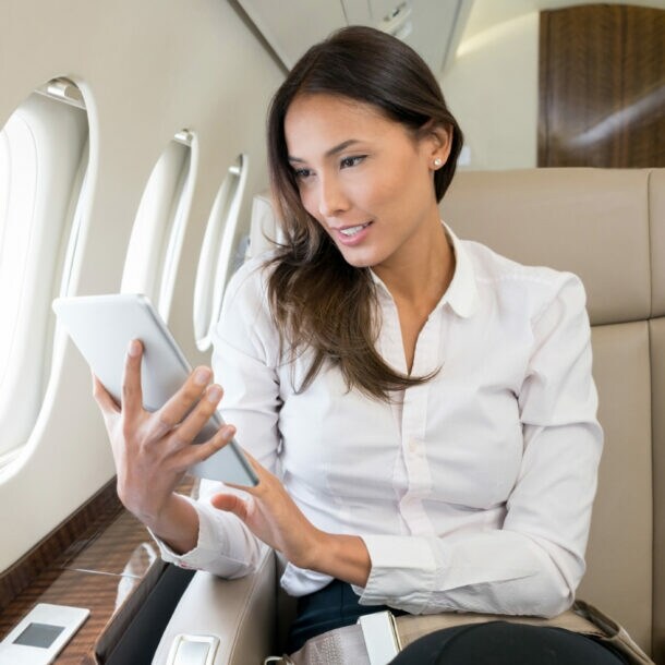 Geschäftsfrau sitzt auf einem Business-Platz im Flugzeug und blickt auf ein Tablet.