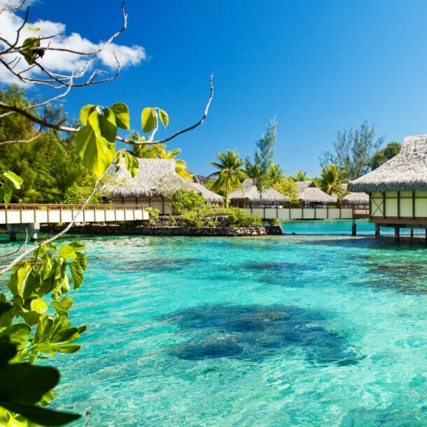 Überwasserbungalows mit Strohdächern über klarem, türkisfarbenem Wasser unter blauem Himmel