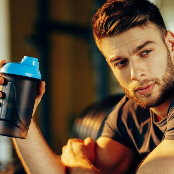 Ein Mann in Sportkleidung hält einen Protein-Shaker in der Hand.