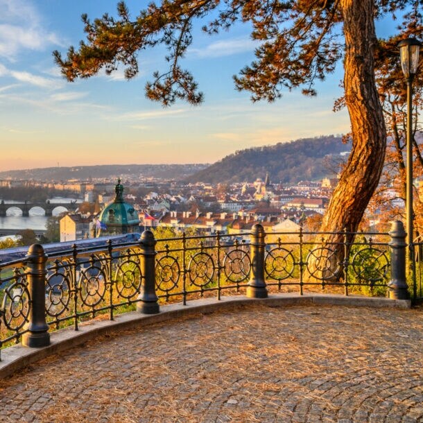 Blick auf die Moldau mit mehreren Brücken und der Altstadt von Prag im Sonnenuntergang, von einer Aussichtsplattform mit schmiedeeisernem Geländer