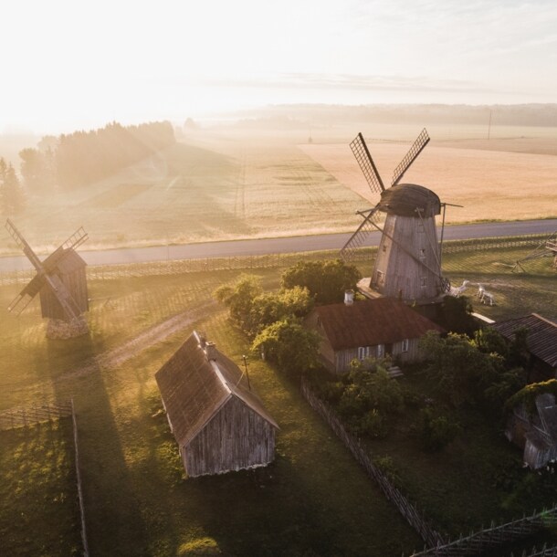 Ein ländliches Gebiet mit drei Windmühlen, Häusern und viel Grün im Sonnenschein.