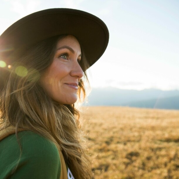 Eine junge Frau mit Hut schaut auf einer Wanderung in die Ferne