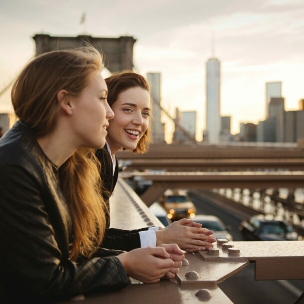 Zwei junge Mädchen stehen lächelnd auf der Brooklyn Bridge vor der Skyline Manhattans