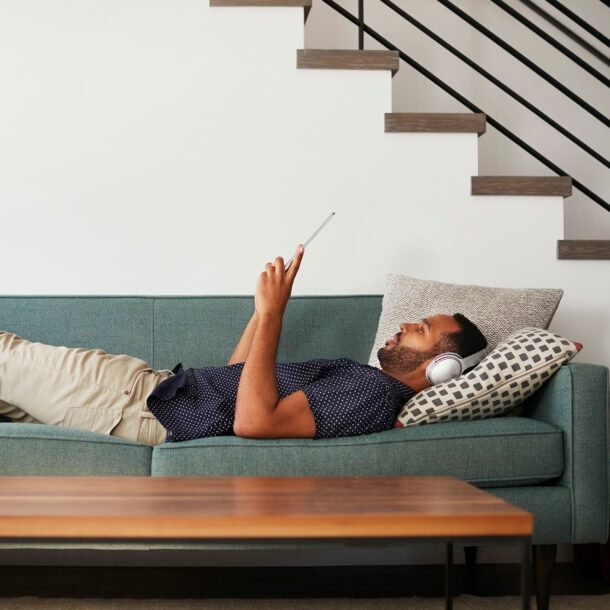 Ein Mann liegt mit Kopfhörern über den Ohren auf einem Sofa und liest.