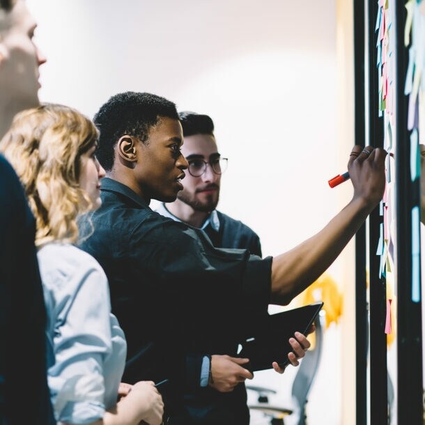 Eine Gruppe von Kolleg:innen steht am Whiteboard und erarbeitet in einem Workshop die Frage nach dem Warum.
