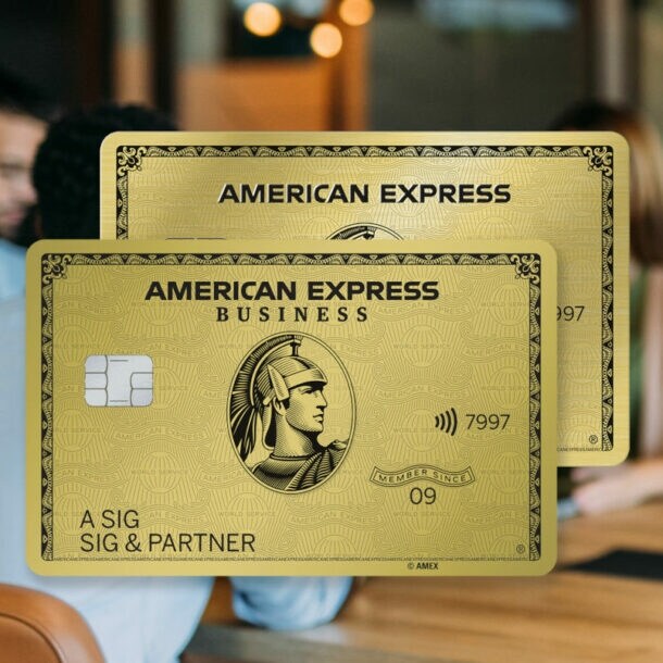 Eine Geschäftsfrau mit Klemmbrett in den Händen lehnt an einem Konferenztisch mit Personen in einem modernen Büro und schaut zufrieden in die Ferne, daneben eine Collage zweier Freisteller von goldenen Kreditkarten von American Express.