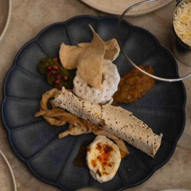 Ein blauer Teller mit verschiedenen indischen Gerichten: Reis in einer Schüssel, Papadam, Chutney, frittiertes Gemüse und ein gerolltes Fladenbrot.