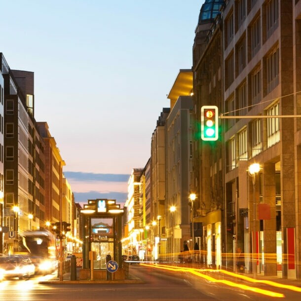 Fotografie mit langer Belichtungszeit einer befahrenen Straße während der Abenddämmerung, der Fokus liegt auf einer grünen Ampel.