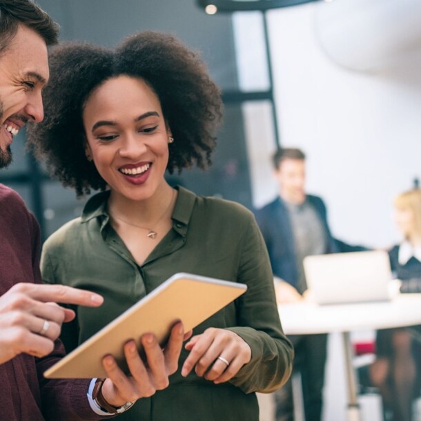 Zwei Kollegen stehen zusammen und schauen gemeinsam auf ein Tablet in einem Büro.