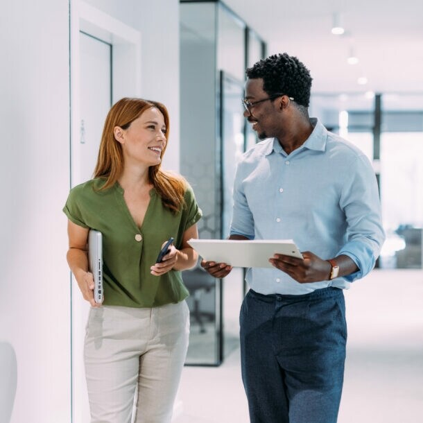 Eine Frau und ein Mann mit Tablets in den Händen kommunizieren auf einem hellen Flur.