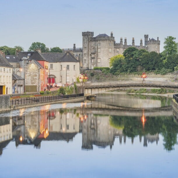 Blick auf Kilkenny mit Kilkenny Castle und der John’s Bridge vor dem Fluss Nore, indem sich die Lichter und Gebäude siegeln.