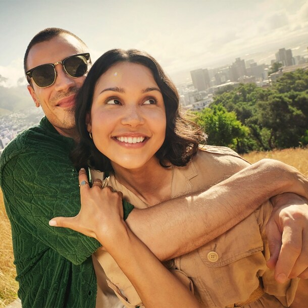 Ein sich umarmendes, junges Paar auf einem Hügel vor der Skyline von Kapstadt.