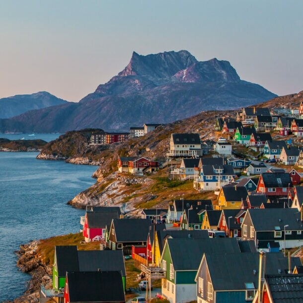 Bunte Häuser der grönländischen Hauptstadt Nuuk an einem Hang, der zum Wasser hin abfällt, im Hintergrund sind Berge.