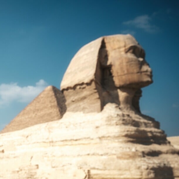 Eine Frau mit Hut fotografiert die Große Sphinx von Gizeh mit einem Smartphone bei klarem Himmel.