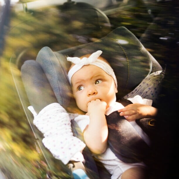 Kind sitzt auf dem Rücksitz eines Autos, hält ein Taschentuch und trägt eine weiße Bluse mit schwarzen Punkten.