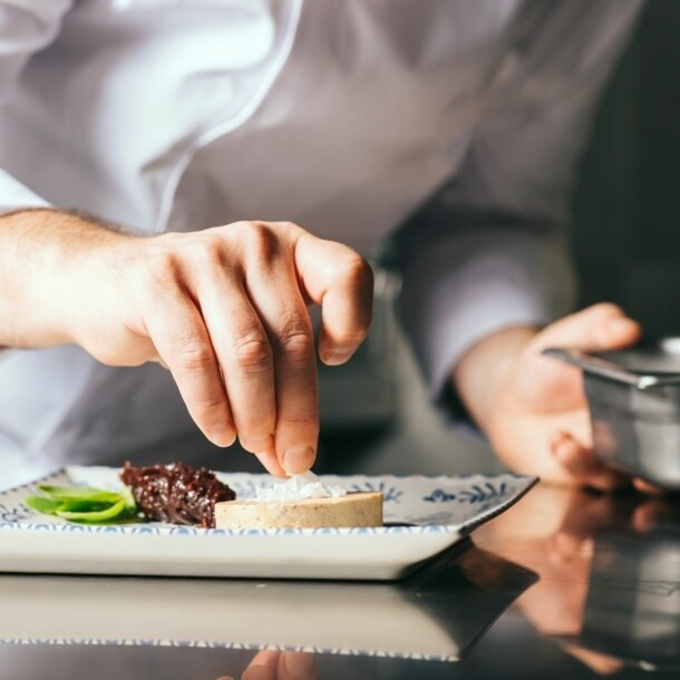 Hand eines Kochs, der einen Teller zubereitet.