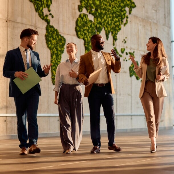 Vier Personen in Business-Outfits kommunizieren nebeneinander gehend in einem Foyer.