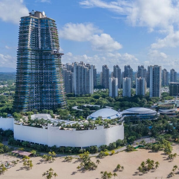Blick auf eine moderne Küstenstadt in Ägypten mit hohem, runder Turm im Bau, mehreren Hochhäusern und einem Sandstrand am Meer.