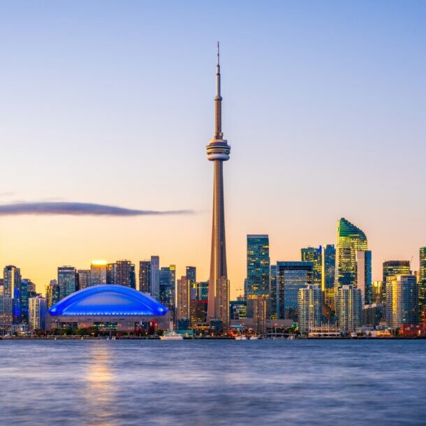 Skyline von Toronto mit Hochhäusern und Fernsehturm am Wasser im Abendlicht.