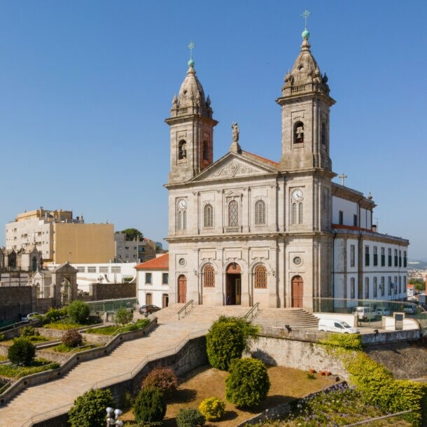 Kirche mit Zwillingstürmen auf einem Hügel über den Dächern einer südländischen Großstadt unter blauem Himmel.