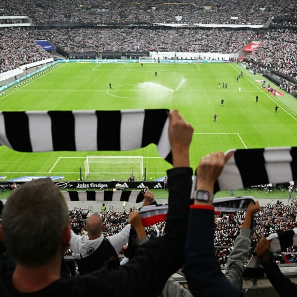 Rückansicht von Personen, die schwarz-weiß gestreifte Schals hochhalten in einem gefüllten Fußballstadion.