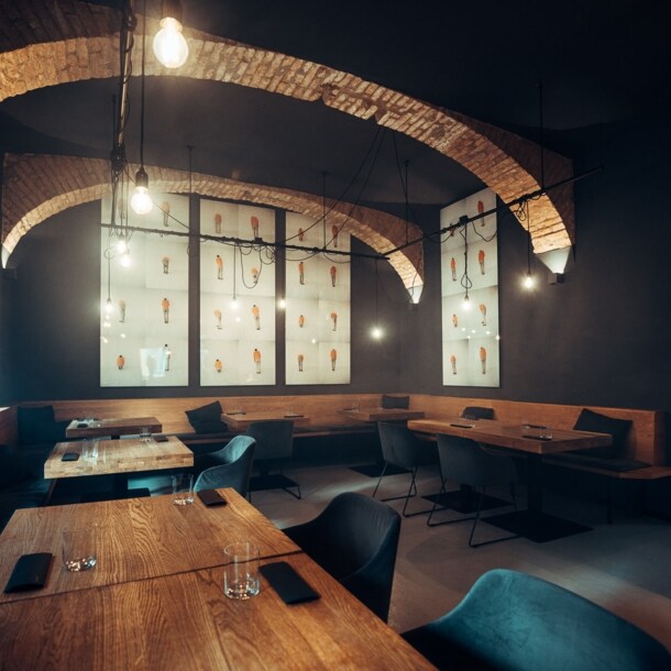 Moderner Speisesaal mit eingedeckten Holztischen und dunklen Wänden mit Gewölbedecke.
