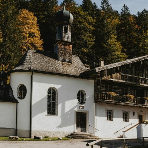 Traditionelles, bayerisches Gasthaus mit Kapelle vor einem Waldgebiet.