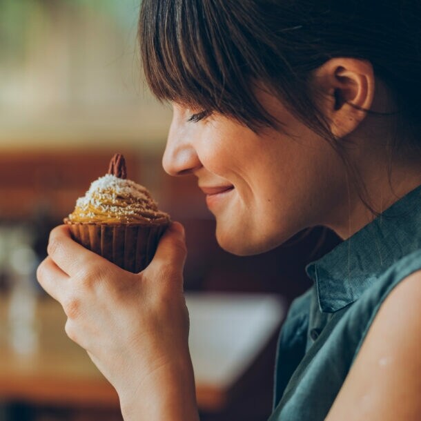 Eine Frau hält sich einen Nuss-Muffin an die Nase und lächelt, ihre Augen sind geschlossen.