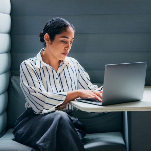 Eine Frau mit Laptop vor sich auf dem Tisch in einer gepolsterten Sitzecke.